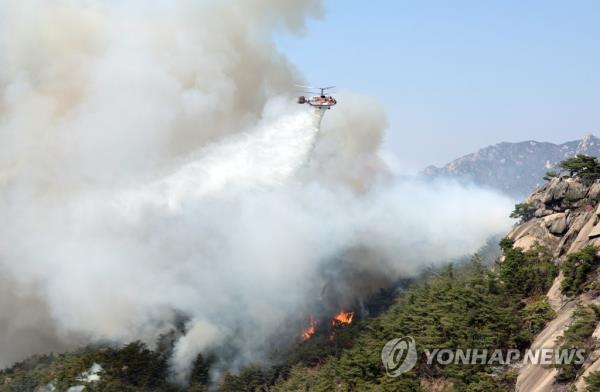A Natio<em></em>nal Fire Agency helicopter dumps water to co<em></em>ntain a fire at Mount Inwang in central Seoul on April 2, 2023. (Yonhap)