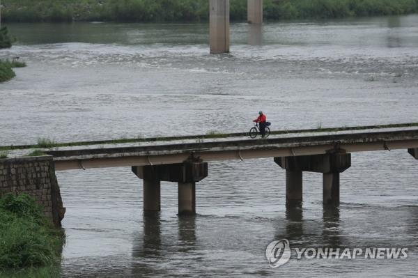 A man rides a bicycle across a bridge over the rising Jungnang Stream in Seoul on July 11, 2023, amid torrential rains. (Yonhap) 