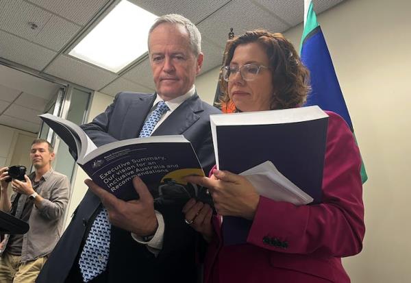 A man and a woman stand side by side reading a big official book