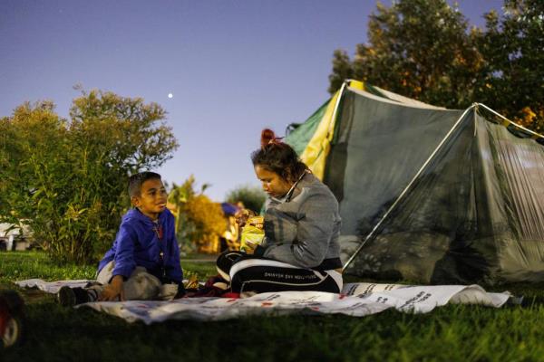Frangeny Mendoza, 27, and her son Ediomar Mendoza, 8, both from Venezuela, eat chips before sleeping in a park across the street from the 22nd District Chicago police station, Oct. 10, 2023.