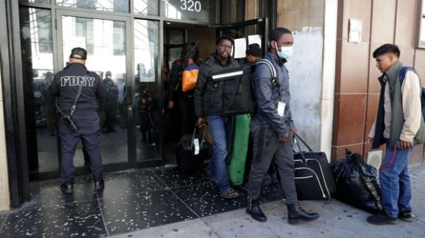 Unidentified migrants carrying their belo<em></em>ngs are pictured exiting the Touro College building located at 320W 31st Street in Midtown Manhattan. The building was being used to house single male migrants, but earlier today October 23, 2023, State and FDNY Fire Marshalls descended into the building and shut down the makeshift shelter and ordered cleared by the end of the day. It's unclear how the building became a shelter and who authorized without FDNY approval. A FDNY Inspector is seen placing the vacate notice at left. (Luiz C. Ribeiro for NY Daily News)